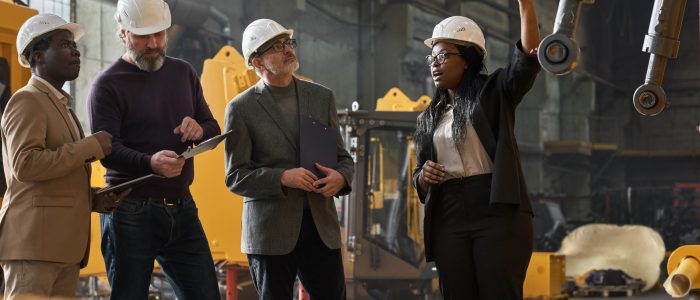 African businesswoman in work helmet presenting the new machine to business people at factory